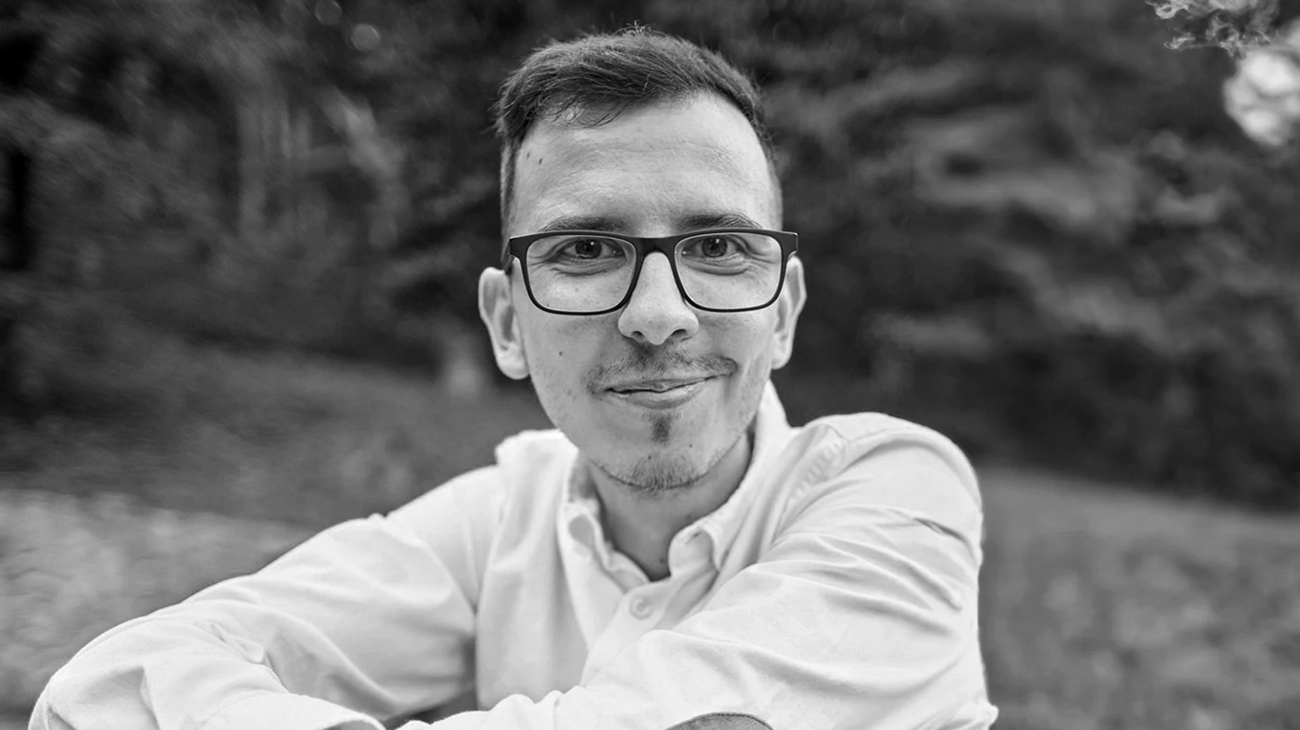Black and white portait of Daniel, the founder, wearing glasses and shirt in a park.